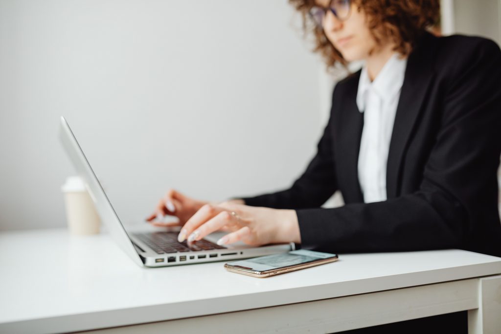 Typing with smartphone near Employee using an AI chatbot on a laptop